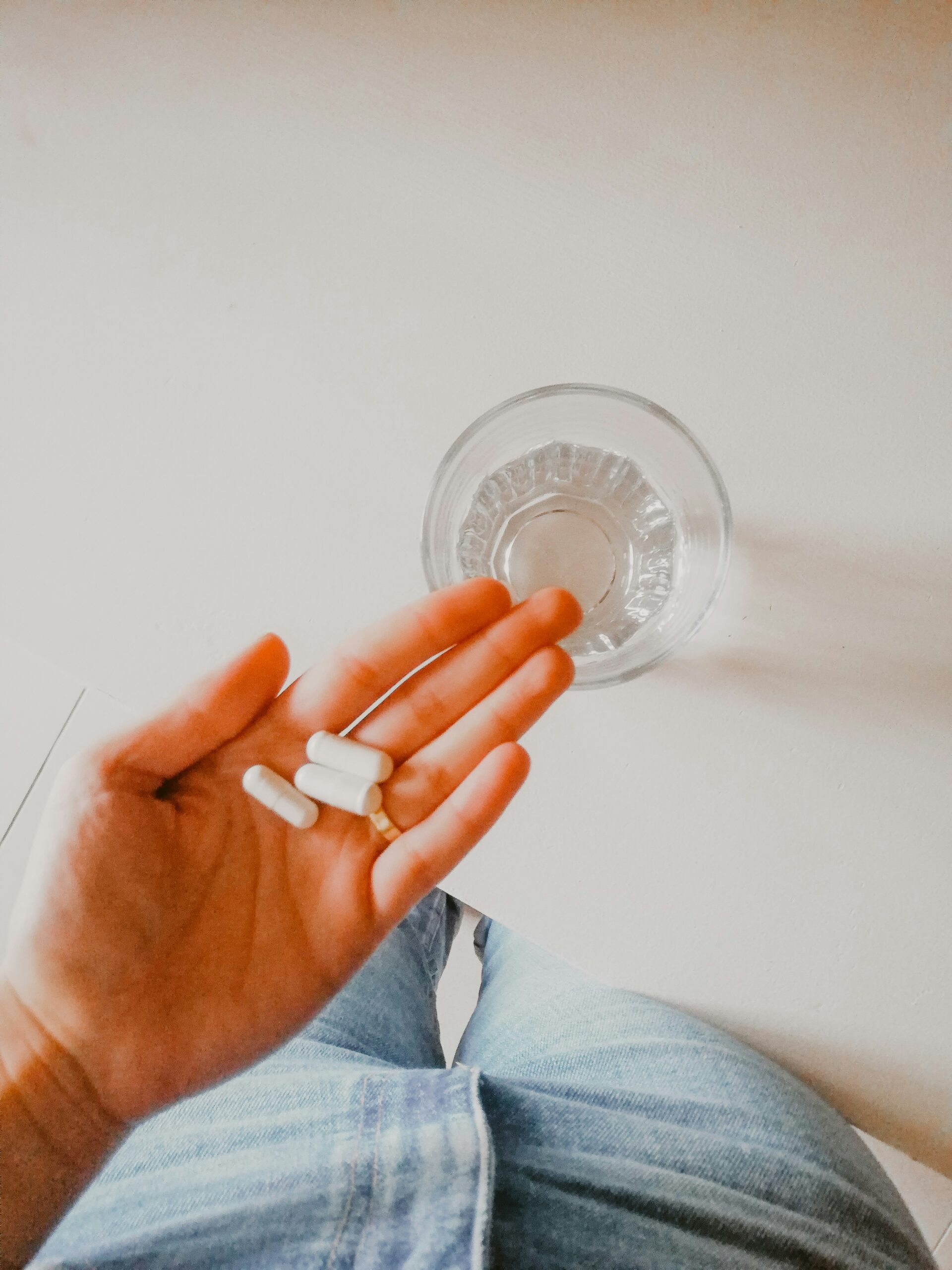 woman holding 3 supplement pills in her hand over a glass of water